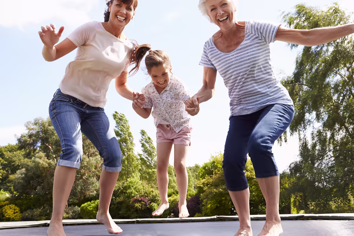 Grandmother, mother, and young girl jumping together on a trampoline