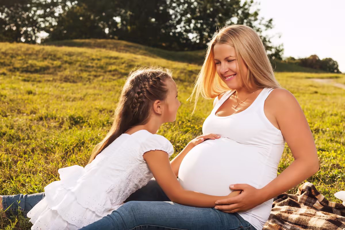 Pregnant mother smiling with her daughter outdoors