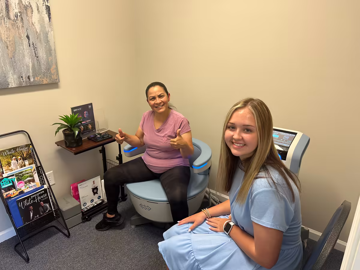 Smiling patient seated on the Emsella chair with a Wave It Away staff member